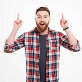 portrait-of-excited-bearded-man-in-checkered-shirt-pointing-fingers-up-over-white-back